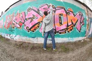 A young guy in a gray hoodie paints graffiti in pink and green c photo