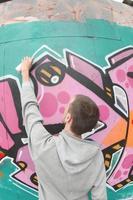 un joven con una sudadera con capucha gris pinta graffiti en rosa y verde c foto