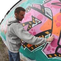 A young guy in a gray hoodie paints graffiti in pink and green c photo