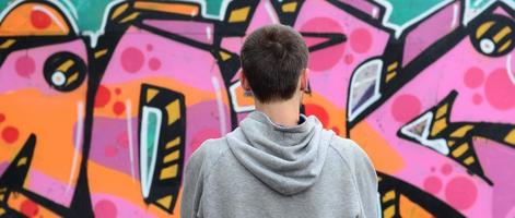 A young graffiti artist in a gray hoodie looks at the wall with photo