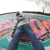 un joven con una sudadera con capucha gris pinta graffiti en rosa y verde c foto