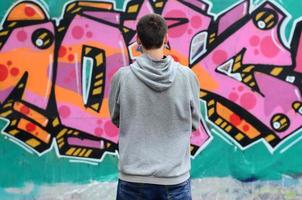 A young graffiti artist in a gray hoodie looks at the wall with photo