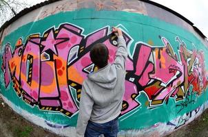 A young guy in a gray hoodie paints graffiti in pink and green c photo