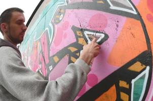 A young guy in a gray hoodie paints graffiti in pink and green c photo