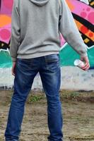 A young graffiti artist in a gray hoodie looks at the wall with photo