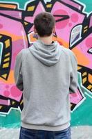 A young graffiti artist in a gray hoodie looks at the wall with photo