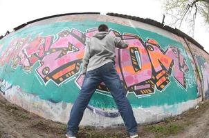 A young guy in a gray hoodie paints graffiti in pink and green c photo