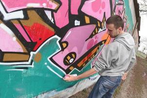 un joven con una sudadera con capucha gris pinta graffiti en rosa y verde c foto