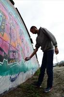 A young guy in a gray hoodie paints graffiti in pink and green c photo