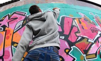 A young guy in a gray hoodie paints graffiti in pink and green c photo