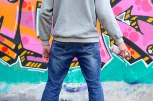 A young graffiti artist in a gray hoodie looks at the wall with photo