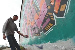 A young guy in a gray hoodie paints graffiti in pink and green c photo