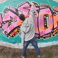 A young guy in a gray hoodie paints graffiti in pink and green c photo