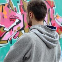 A young graffiti artist in a gray hoodie looks at the wall with photo