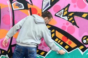 A young guy in a gray hoodie paints graffiti in pink and green c photo