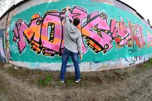 A young guy in a gray hoodie paints graffiti in pink and green c photo