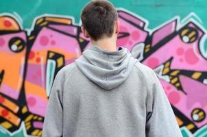 A young graffiti artist in a gray hoodie looks at the wall with photo