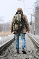 A man with a large backpack goes ahead on the railway track duri photo