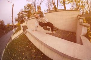 un joven realiza un salto a través del parapeto de hormigón. el atleta practica parkour, entrenando en condiciones de calle. el concepto de subculturas deportivas entre los jóvenes foto