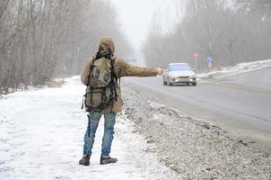 un hombre con una mochila grande que muestra los pulgares hacia arriba para hacer autostop du foto