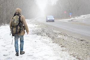 un hombre con una mochila grande camina por una carretera asfaltada suburbana foto