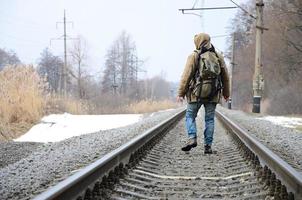 A man with a large backpack goes ahead on the railway track duri photo