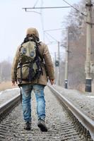 A man with a large backpack goes ahead on the railway track duri photo