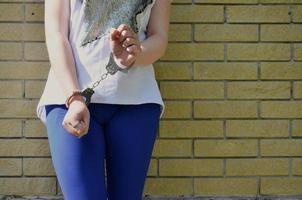 Fragment of a young criminal girl's body with hands in handcuffs against a yellow brick wall background. The concept of detaining an offender of a female criminal in an urban environment photo