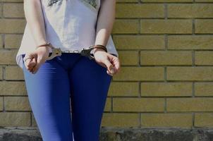 Fragment of a young criminal girl's body with hands in handcuffs against a yellow brick wall background. The concept of detaining an offender of a female criminal in an urban environment photo