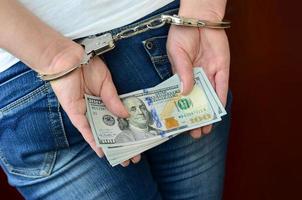 An arrested girl with handcuffed hands with a huge amount of dollar bills. Back view photo