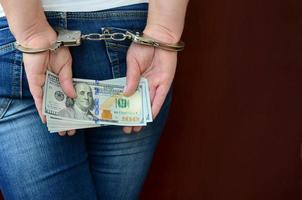 An arrested girl with handcuffed hands with a huge amount of dollar bills. Back view photo