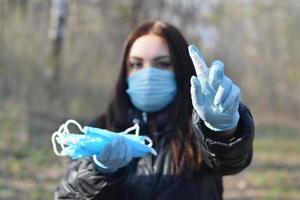 mujer joven con máscara protectora muestra botellas de spray desinfectante y máscaras faciales protectoras al aire libre en madera de primavera foto