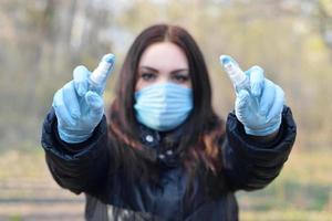 Young woman in protective mask shows sanitizer spray bottles outdoors in spring wood photo