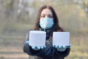 Covidiot concept. Young woman in protective mask holds many rolls of toilet paper outdoors in spring wood photo