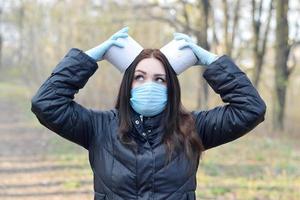 Covidiot concept. Young woman in protective mask holds many rolls of toilet paper outdoors in spring wood photo