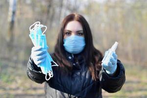 Young woman in protective mask shows sanitizer spray bottles and protective face masks outdoors in spring wood photo