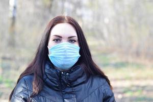 Portrait of young brunette woman in blue protective mask outdoors in spring wood photo