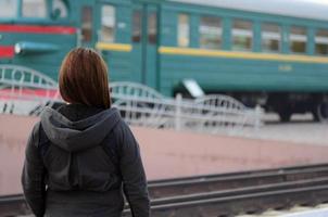 A young red-haired girl is standing on the railway platform and watching the departing train. The woman was late for her train. Back view photo