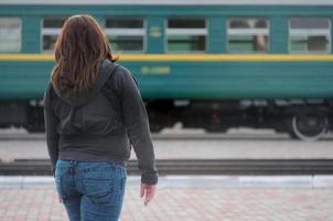 A young red-haired girl is standing on the railway platform and watching the departing train. The woman was late for her train. Back view photo