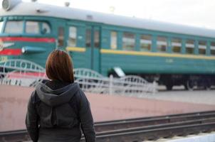 A young red-haired girl is standing on the railway platform and watching the departing train. The woman was late for her train. Back view photo