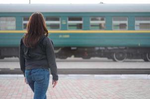 A young red-haired girl is standing on the railway platform and watching the departing train. The woman was late for her train. Back view photo