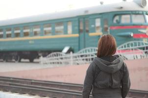 A young red-haired girl is standing on the railway platform and watching the departing train. The woman was late for her train. Back view photo