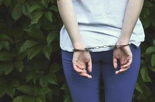 Fragment of a young criminal girl's body with hands in handcuffs against a green blossoming ivy leaves background. The concept of detaining an offender of a female criminal in a rural environment photo