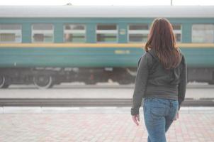 A young red-haired girl is standing on the railway platform and watching the departing train. The woman was late for her train. Back view photo