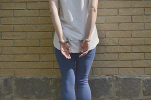 Fragment of a young criminal girl's body with hands in handcuffs against a yellow brick wall background. The concept of detaining an offender of a female criminal in an urban environment photo