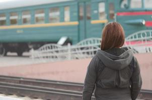 A young red-haired girl is standing on the railway platform and watching the departing train. The woman was late for her train. Back view photo