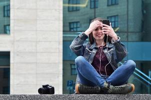 A girl photographer uses a smartphone and sits on a granite para photo