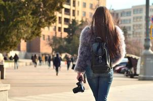 Rear view of a girl with a digital camera on a crowded street ba photo