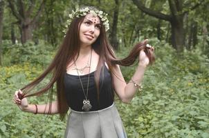 retrato de una joven emocional con una corona floral en la cabeza y adornos brillantes en la frente. linda morena posando en un hermoso bosque floreciente durante el día en un buen día foto