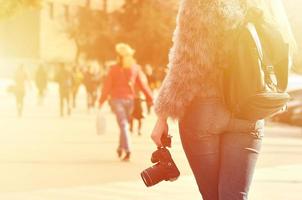 Rear view of a girl with a digital camera on a crowded street ba photo